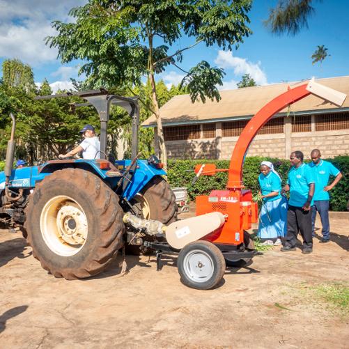 Kobieta prowadzi traktor, którego pracę obserwuje 5 osób, z boku stoi kobieta, która robi zdjęcie traktora