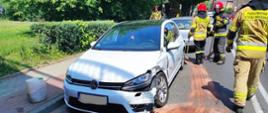 Zdjęcie przedstawia uszkodzoną karoserię białego samochodu marki VW Golf podczas kolizji na ul. Drzymały w Białogardzie. Pojazd widoczny przodem od strony kierowcy. Obok pojazdu strażacy w umundurowaniu specjalnym. Jezdnia wokół pojazdu posypana sorbentem