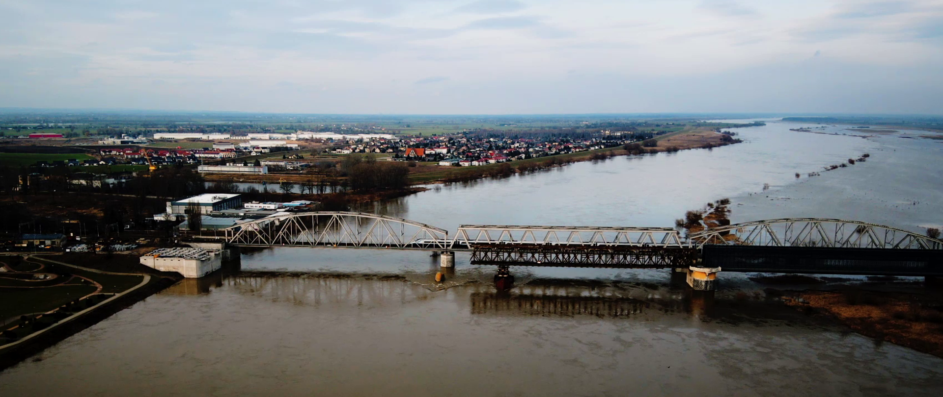 Wisła w okolicach mostu tczewskiego. Po moście przejeżdża pociąg pendolino. Po prawej stronie widoczne zalania, po lewej tereny miasta.