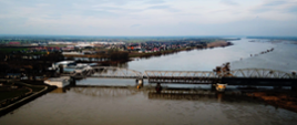 Wisła w okolicach mostu tczewskiego. Po moście przejeżdża pociąg pendolino. Po prawej stronie widoczne zalania, po lewej tereny miasta.