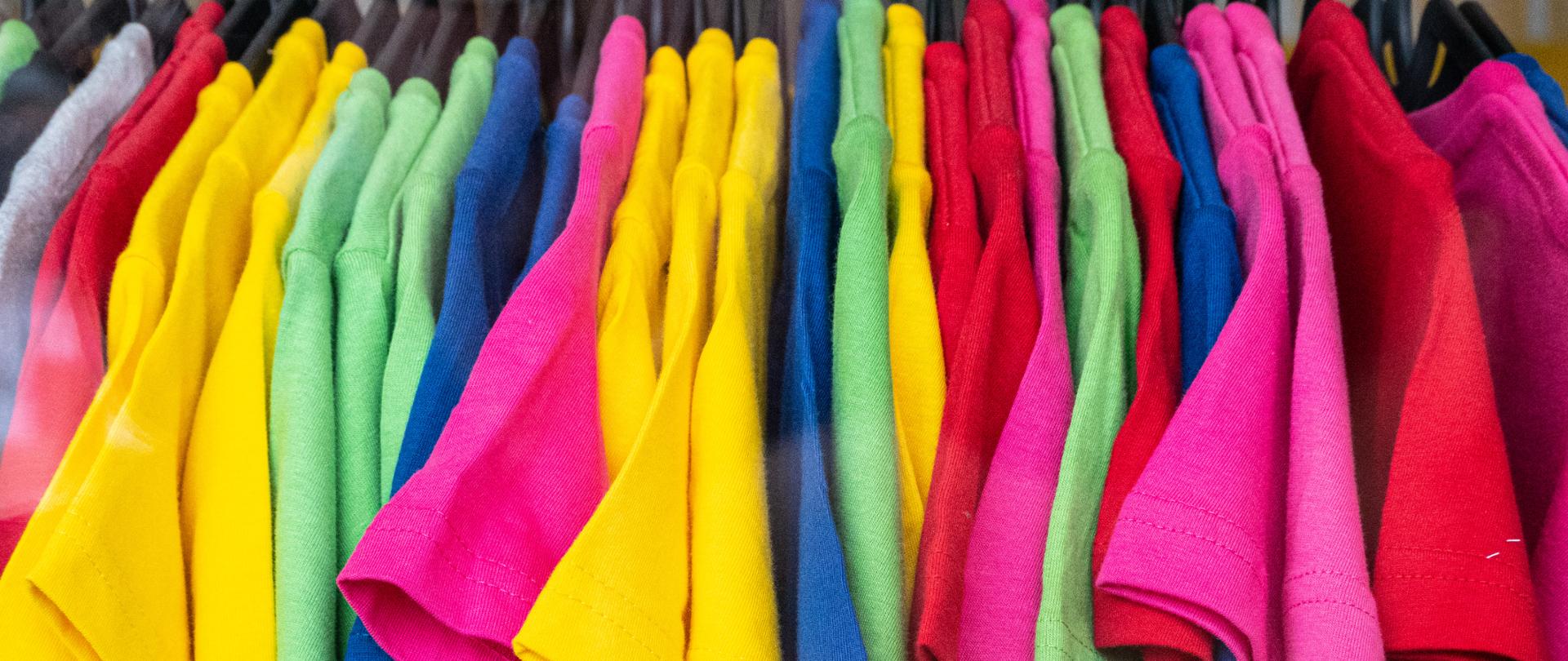Różnokolorowe t-shirty wiszą blisko siebie na długim wieszaku