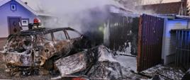 Pożar garażu, czynności dogaszania, wrak zniszczonego samochodu osobowego w wyniku pożaru wyciągnięty z garażu.