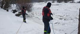 Na zdjęciu dwóch strażaków zabezpiecza linami sanie lodowe na rzece San, na których znajduje się strażak