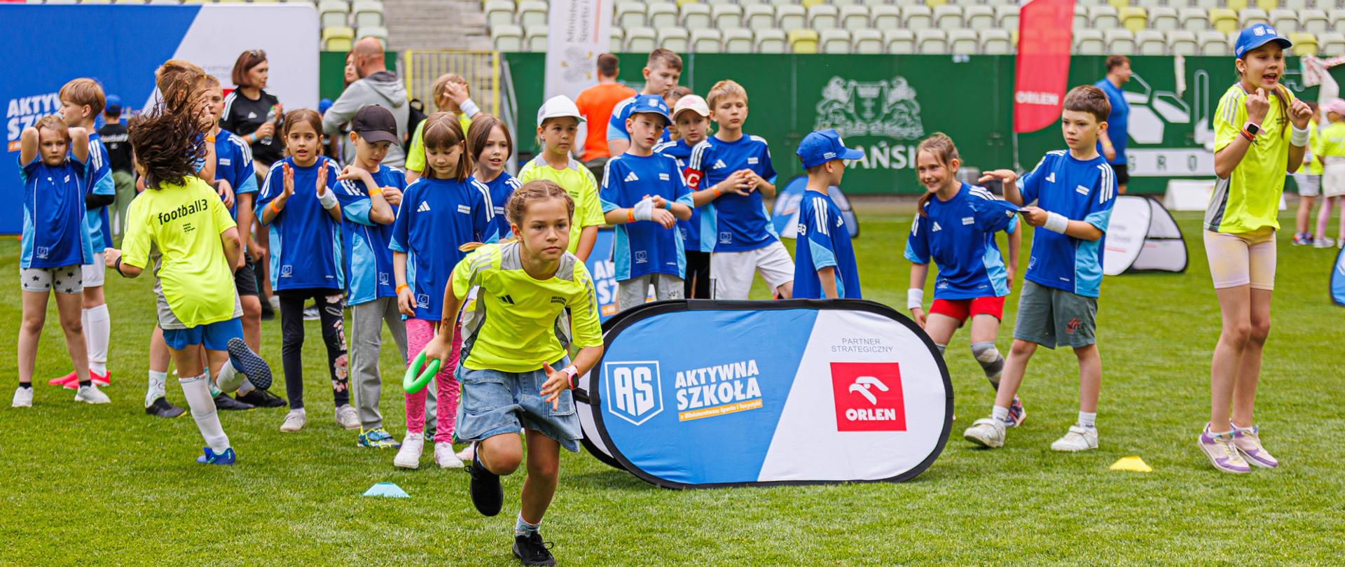 Zabawy dzieci w Aktywną Szkołą na zielonej trawie na stadionie w Gdańsku