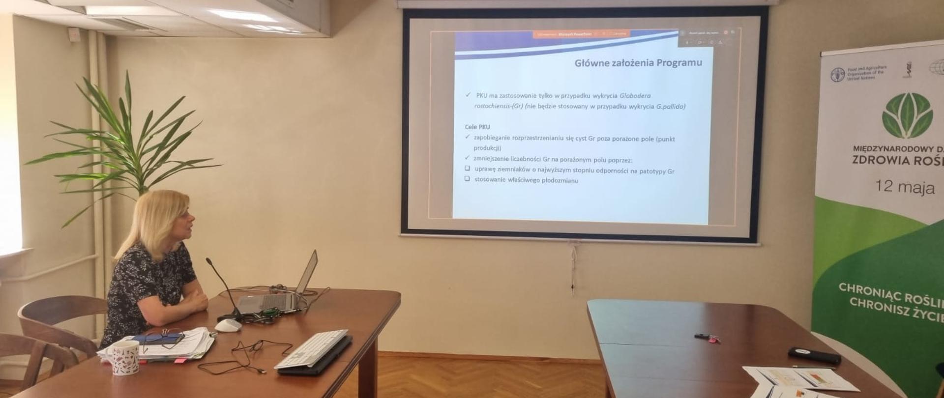 Kierownik Działu Nadzoru Fitosanitarnego siedząca przed laptopem i prowadząca szkolenie. Na ekranie rzutnika wyświetlana jest treść prezentacji.
