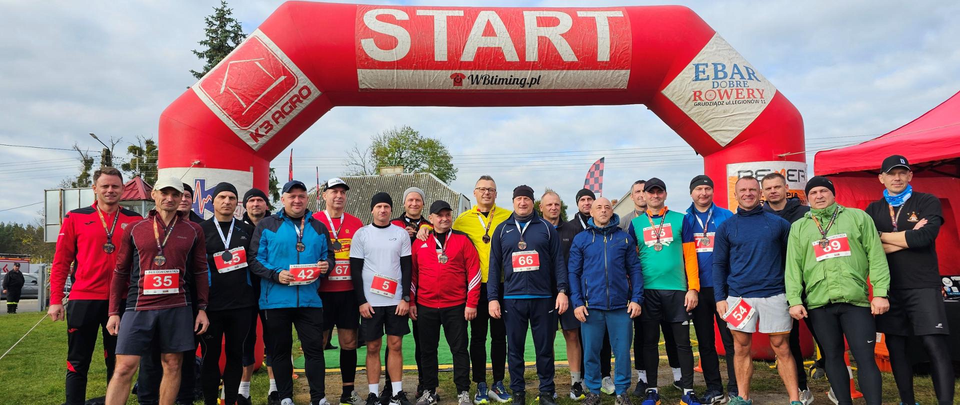 Linia startu biegu, na której do zdjęcia pozuje kilkunastu mężczyzn w strojach sportowych.
