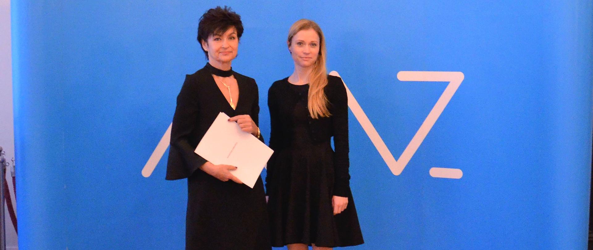 Anna Goławska, zastępca dyrektora Departamentu Funduszy Europejskich i e-Zdrowia oraz Renata Kiempa, prezes szpitala w Miastku pozują do zdjęcia z podpisaną umową na tle niebieskiej ścianki Ministerstwa Zdrowia.