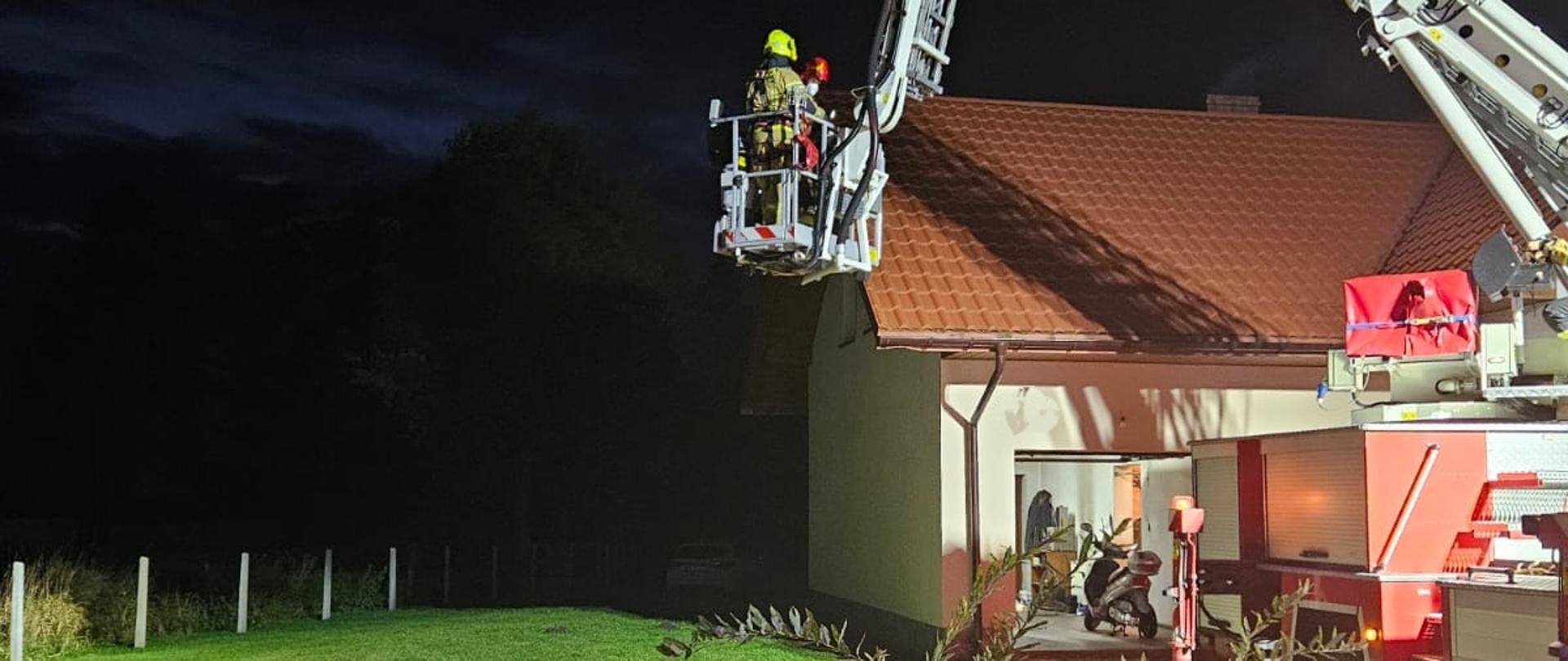 Pora wieczorna. zmrok, sprawiony podnośnik hydrauliczny w pobliżu komina, w koszu podnośnika strażak, który prowadził działania przy gaszeniu sadzy 