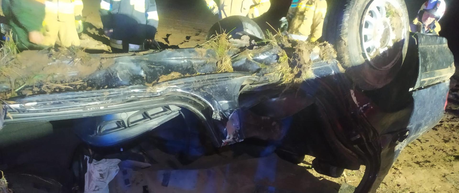 Przewrócony na dach samochód. w tle strażacy.