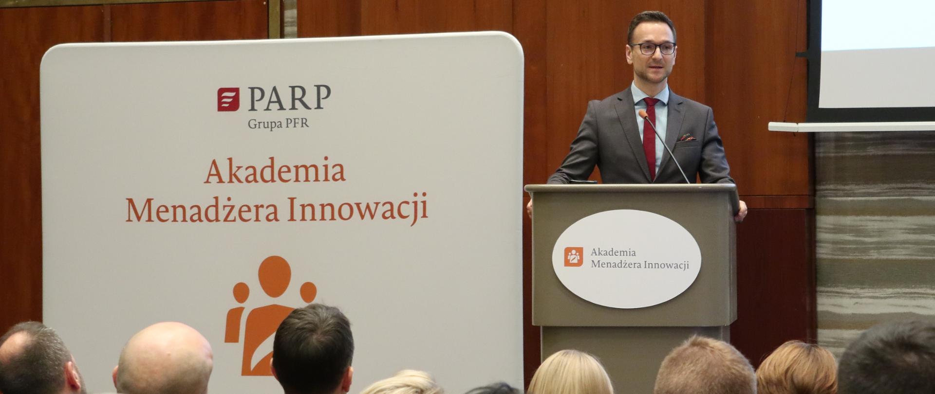 Na zdjęciu wiceminister Waldemar Buda, w tle baner z napisem PARP Akademia Menadżera Innowacji, z przodu siedzą uczestnicy wydarzenia.