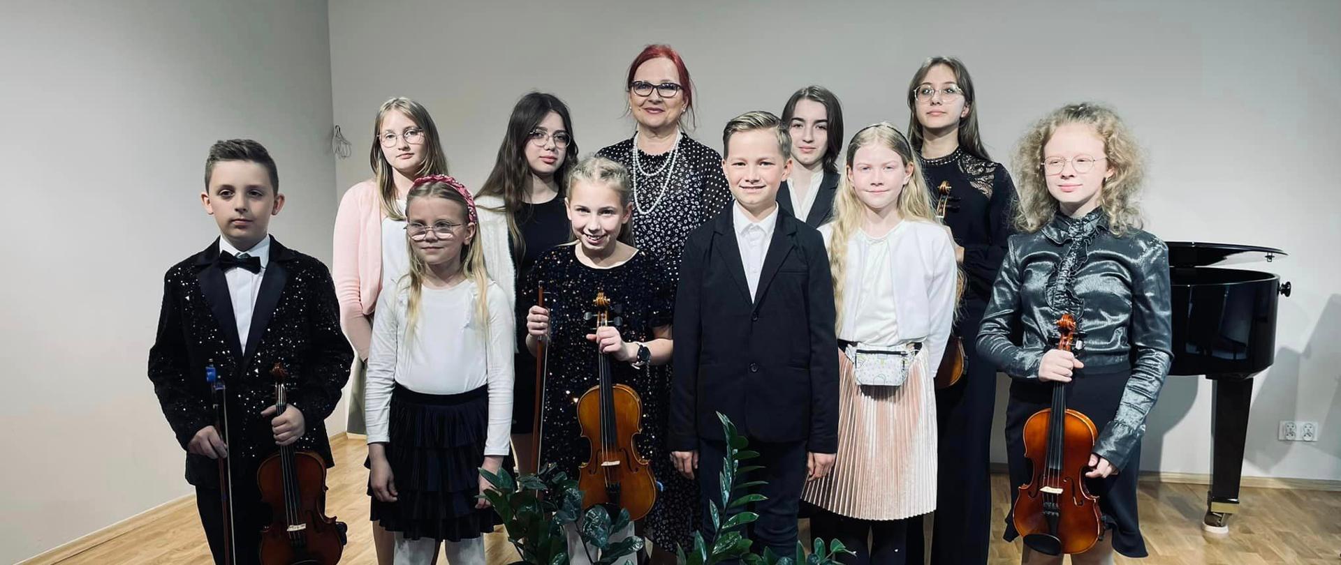 Grupa uczniów wraz z nauczycielami stoi na scenie sali koncertowej