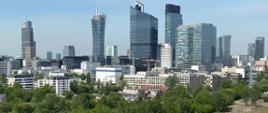 Panorama Warszawy z drzewami na pierwszym planie oraz nowoczesnymi biurowcami w tle.