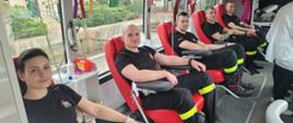 Strażacy siedzący na fotelach w mobilnym autobusie podczas oddawania krwi