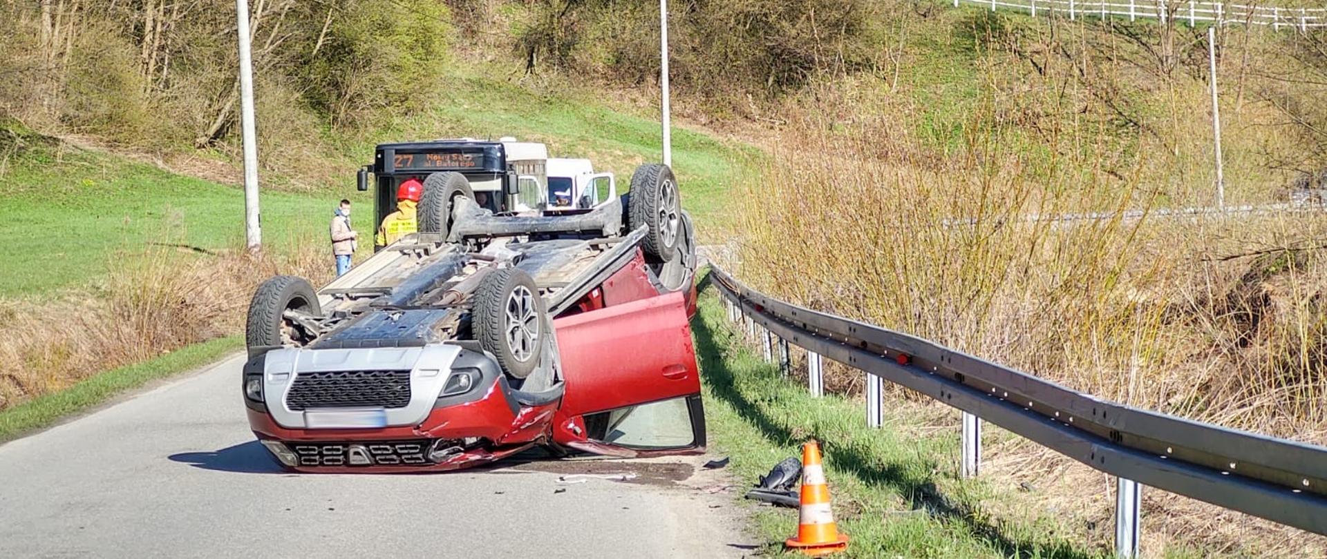 Inne ujęcie samochodu osobowego leżącego na dachu. W tle widać samochody stojące w korku.