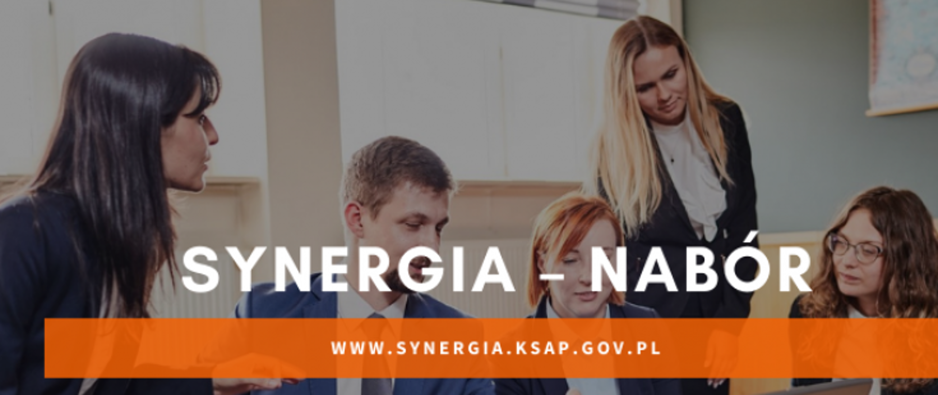 Na zdjęciu 4 dziewczyny 1 chłopak siedzą na kanapie, patrzą na ekran otworzonego laptopa, który jest na stoliku. Wszystkie osoby są elegancko ubrane, w białe koszule i garnitury. Na środku zdjęcia znajduje się napis: Synergia-nabór.