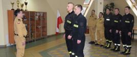 Nowo przyjęci strażacy stoją przed Komendantem Powiatowym.