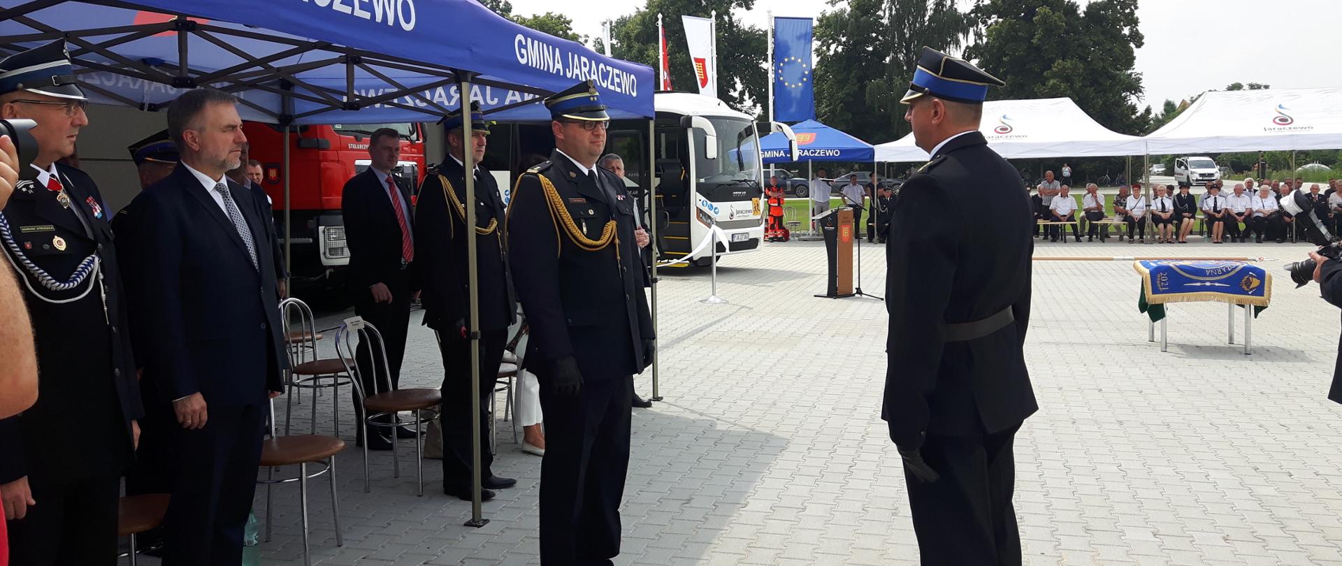 grupa osób stoi pod namiotem. w tle inny namiot z osobami 