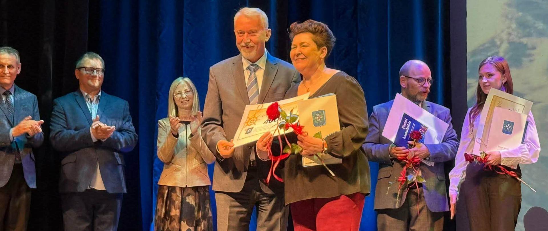 W sali WCK Ewa Rocławska odbiera od prezydenta nagrodę. W tle jury.