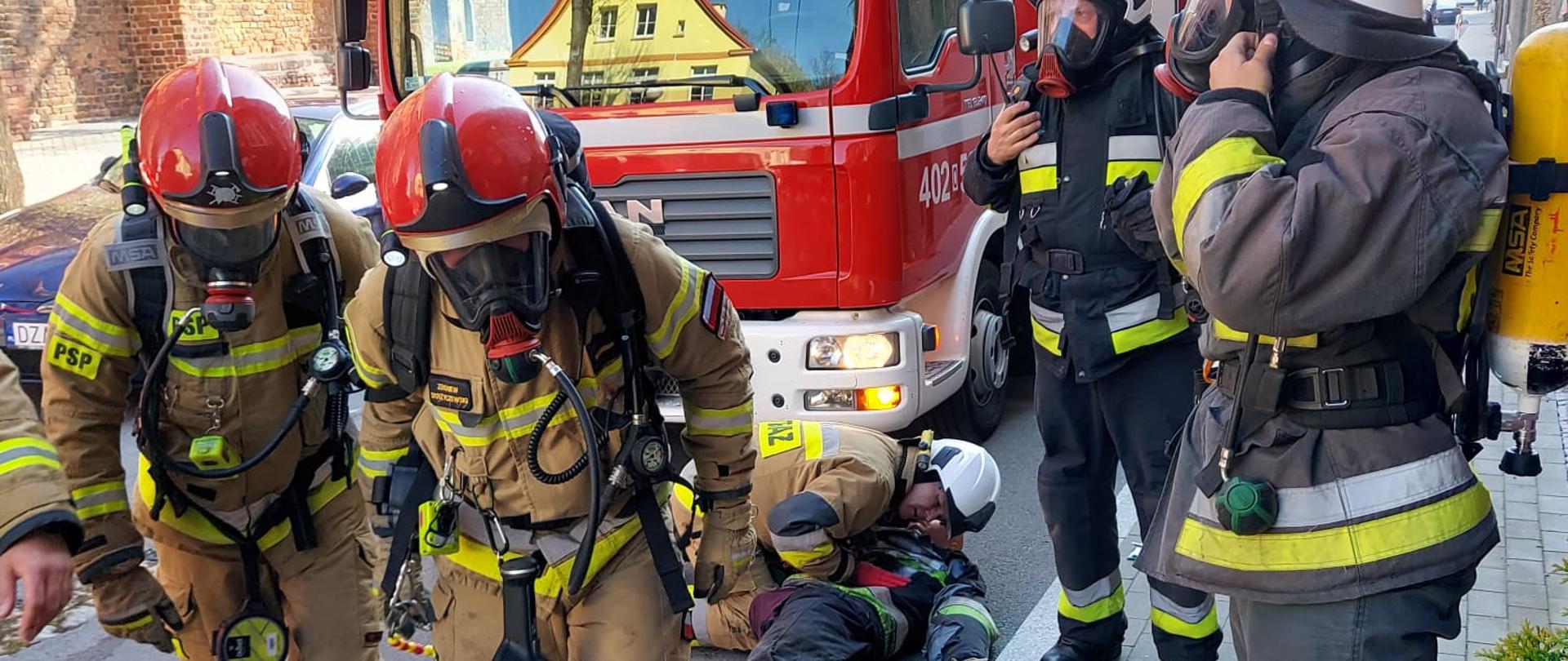 Ćwiczenia na obiekcie DPS Grodków - zdjęcie przedstawia strażaków ubranych w sprzęt ochrony układu oddechowego podczas rozwijania linii gaśniczej