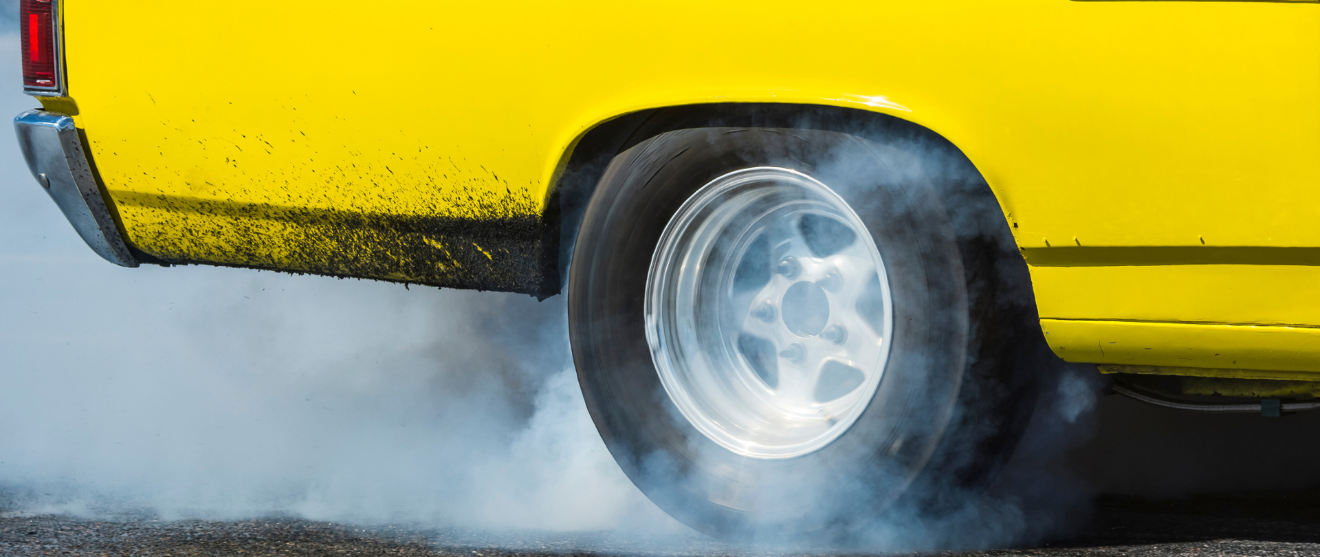 Żółty, nieco brudny samochód, w wąskim ujęciu. Widoczne jest prawe tylne koło, za którym się mocno kurzy