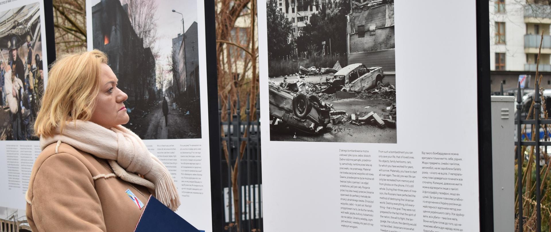 kobieta stoi przed wystawą obrazującą wojnę w Ukrainie