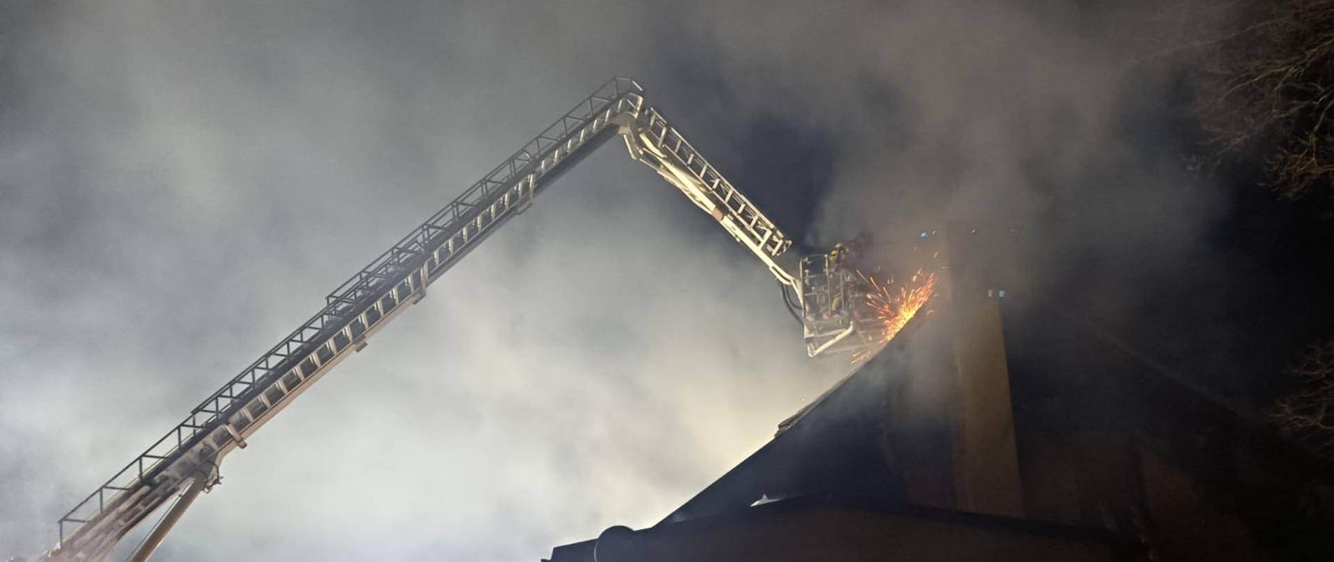 Strażacy na podnośniku rozcinają dach bucynku 