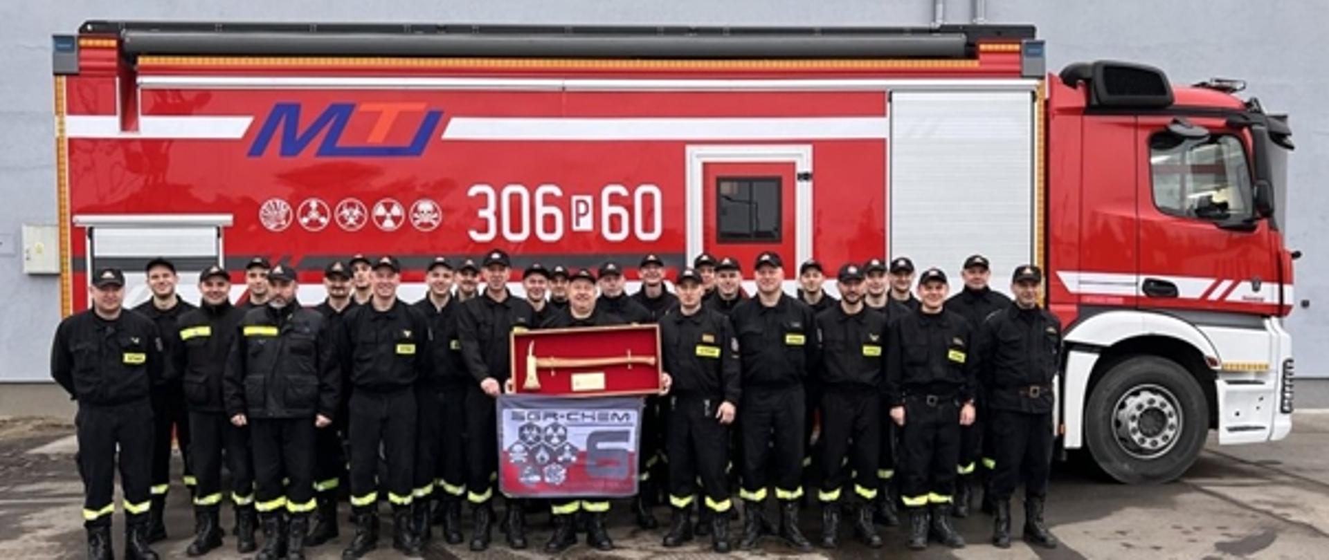 Strażacy na tle samochodu chemicznego z mł. kpt. Piotr Grzebyta