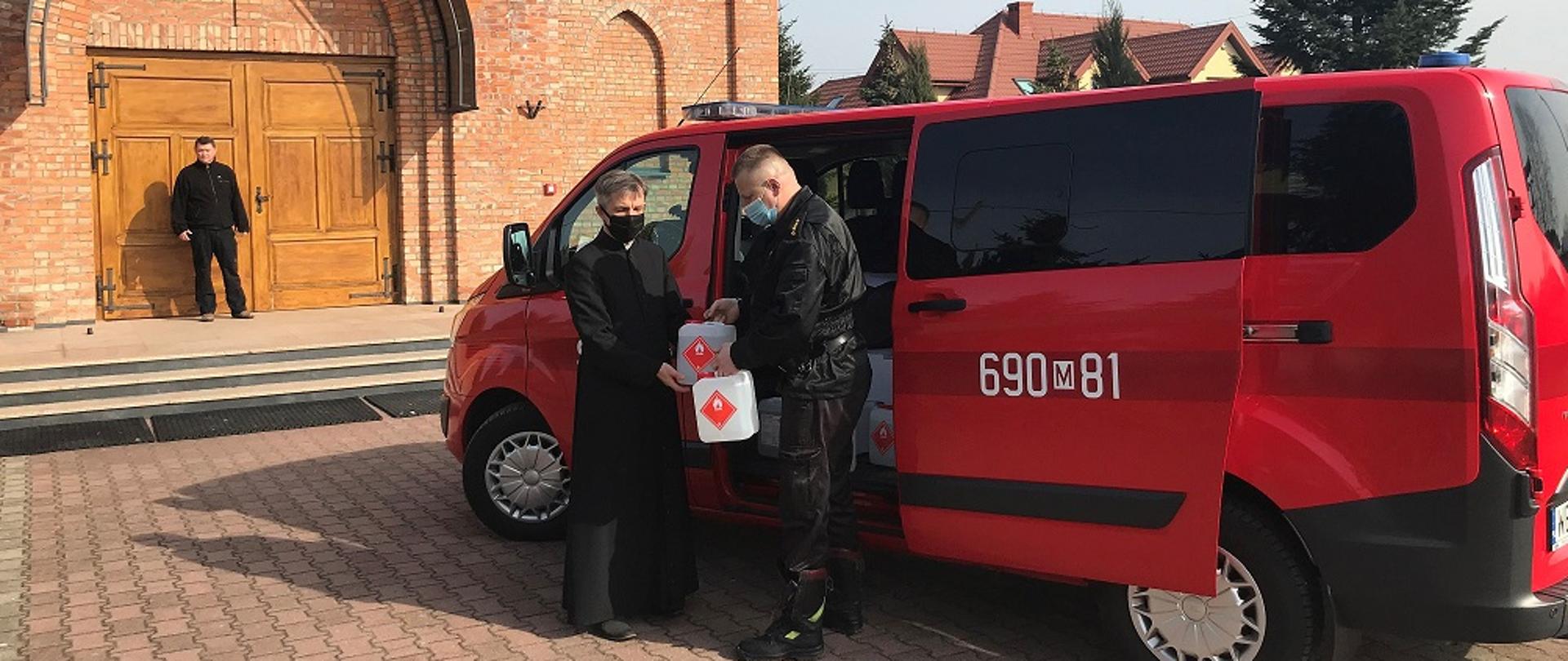 Strażak przekazuje środki ochrony kapłanowi