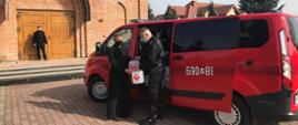 Strażak przekazuje środki ochrony kapłanowi