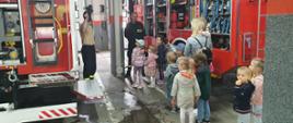 Dzieci i strażacy stoją przy samochodach strażackich. Strażacy opowiadają i pokazują sprzęt. 
