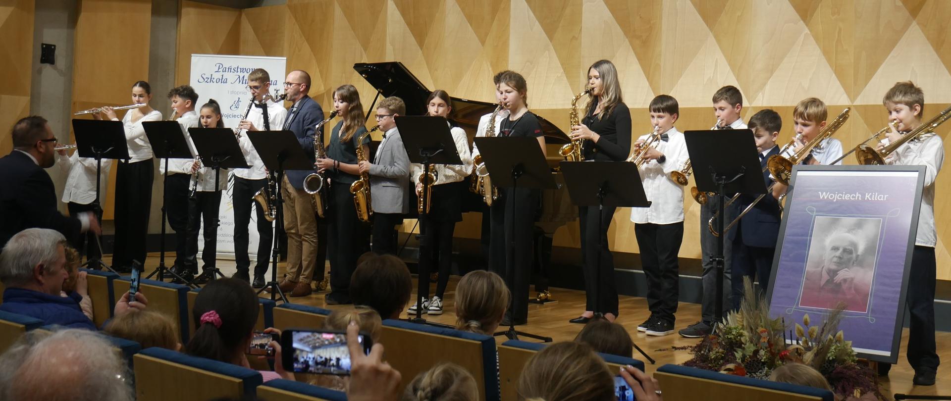 Grupa uczniów z instrumentami dętymi stoi na scenie, zdjęcie Wojciecha Kilara