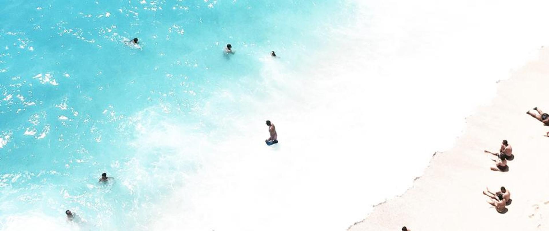 Zdjęcie przedstawia ludzi na plaży i kąpiących się w morzu 