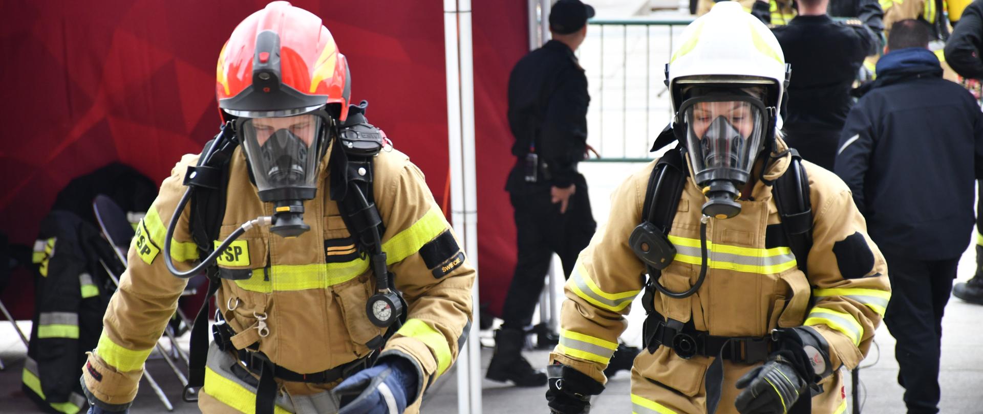 Na zdjęciu widać strażaków w ubraniu bojowym przed wejściem do PKIN ubranych w mundur bojowy w hełmach i aparatach OUO