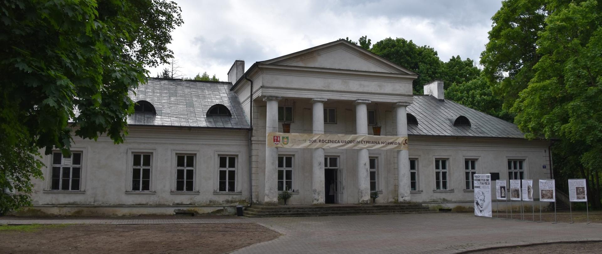 Zdjęcie Pałacu Dębinkach. Budynek biały, parterowy, z licznymi oknami i kolumnadą w wejściu. 