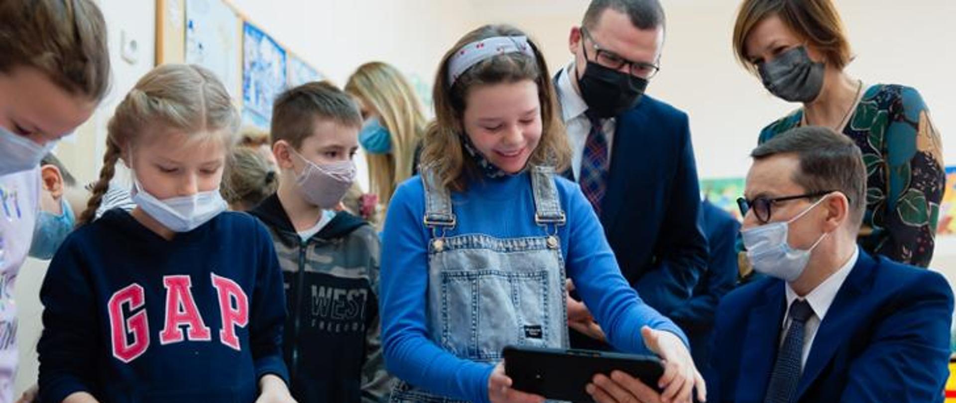 Kilkoro dzieci patrzących na tablet wraz z trojgiem dorosłych