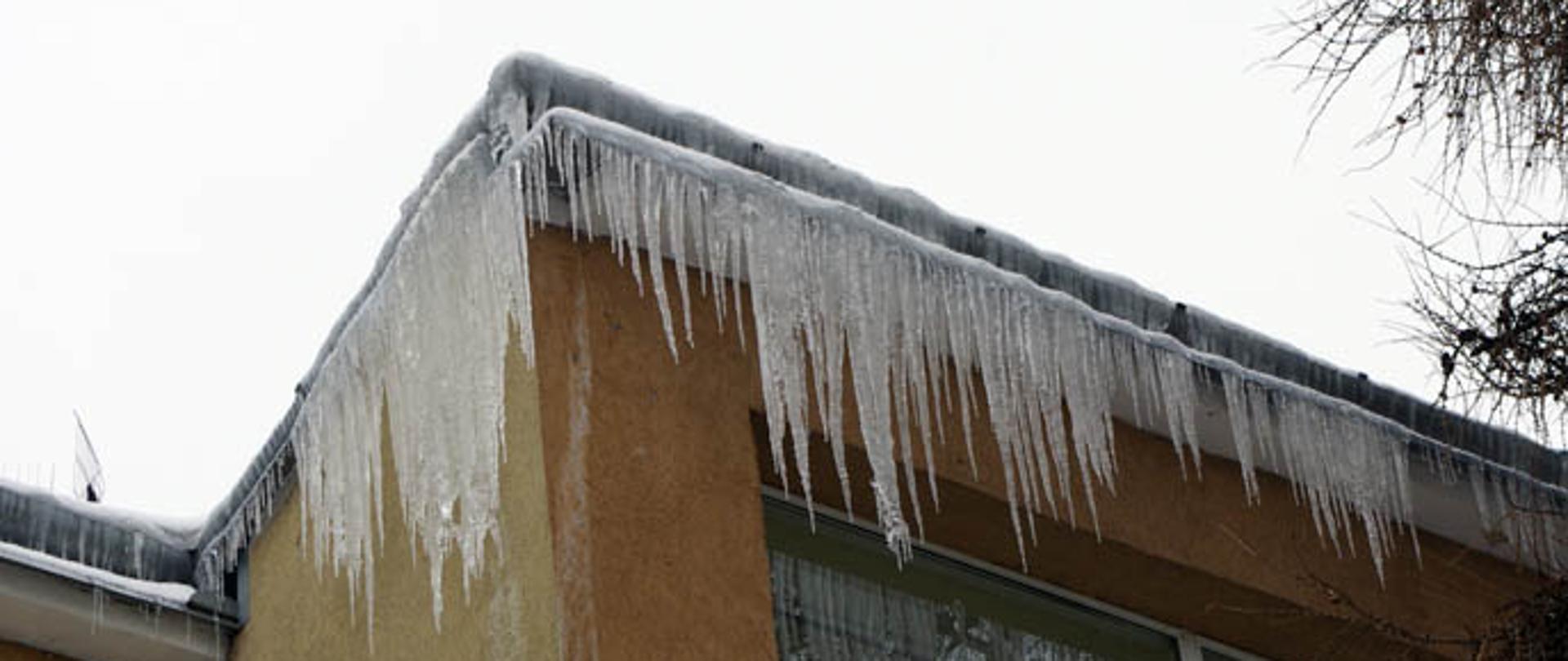 Zdjęcie przedstawiające budynek z oblodzonym dachem i zwisającymi soplami