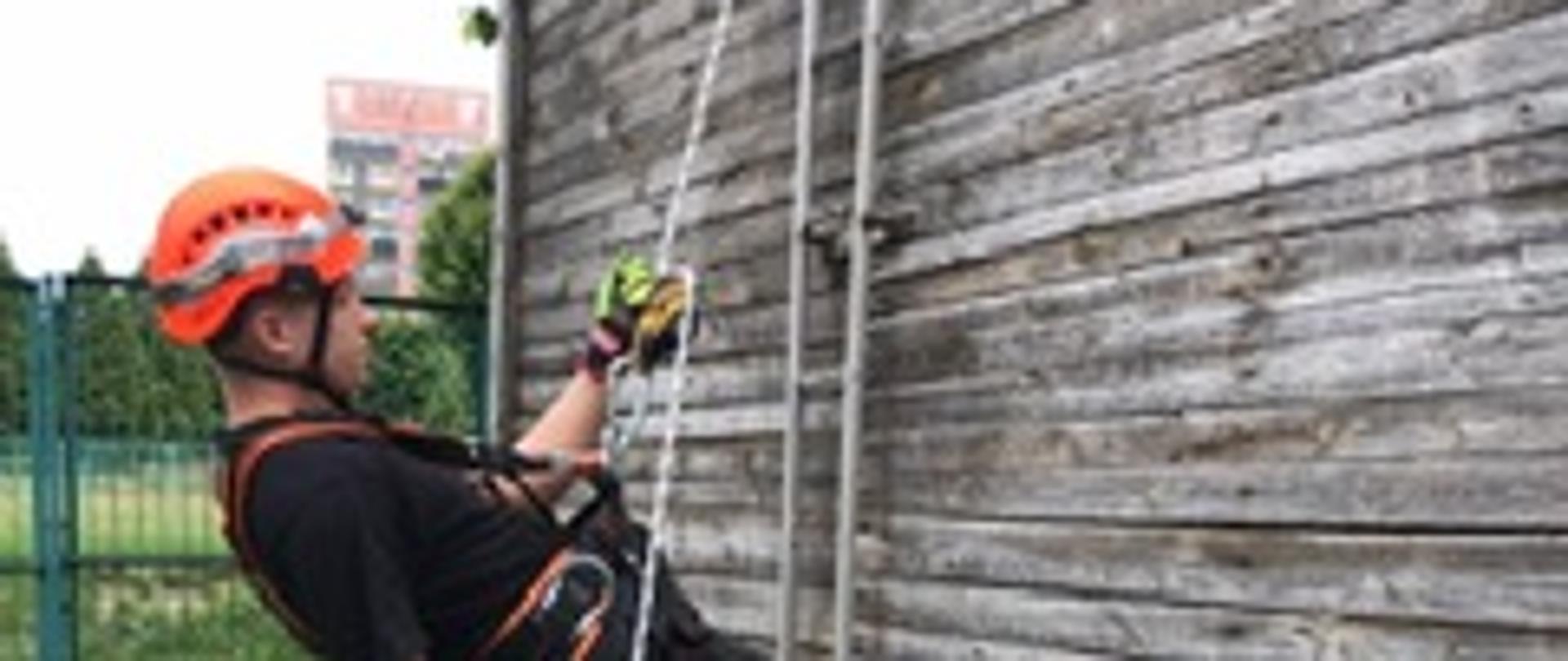 Strażak przypięty przy pomocy urządzenia asekuracyjnego do liny w trakcie zjazdu w dół na i wspinalni.