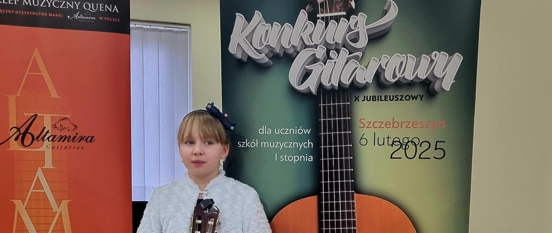 Zdjęcie uczennicy trzymającej instrument na tle rollup-a konkursowego