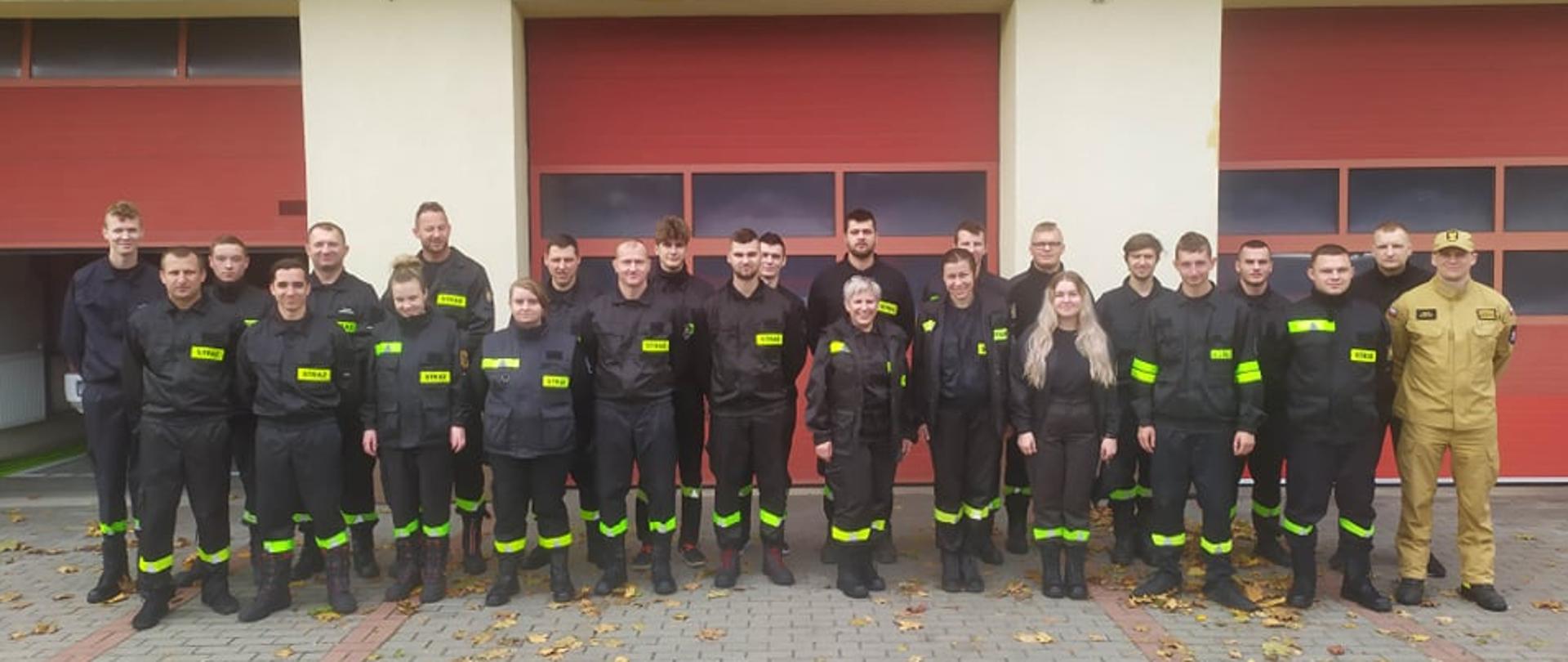 na parkingu przed budynkiem komendy stoją kursanci ubrani w czarne mundury koszarowe. 