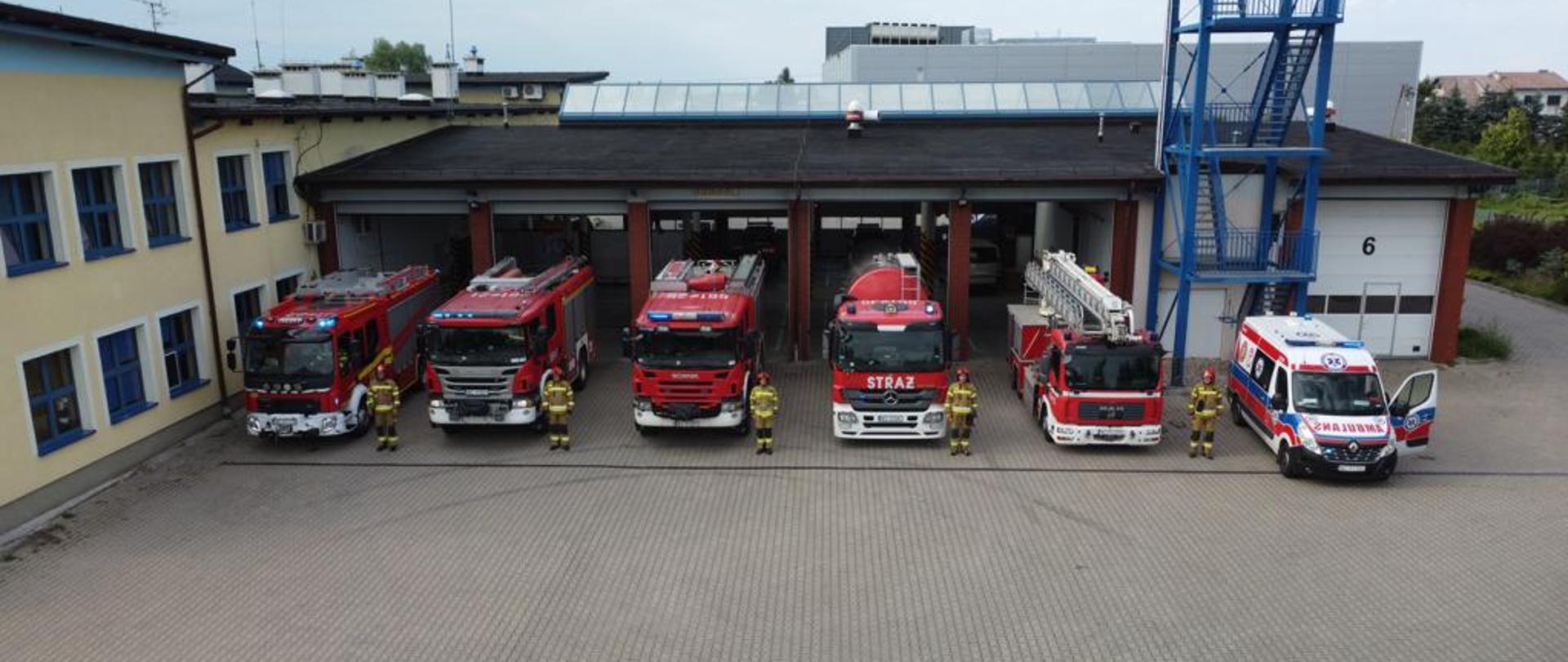 Samochody i strażacy stoją przed garażem JRG w Błoniu podczas wycia syren z okazji rocznicy powstania warszawskiego