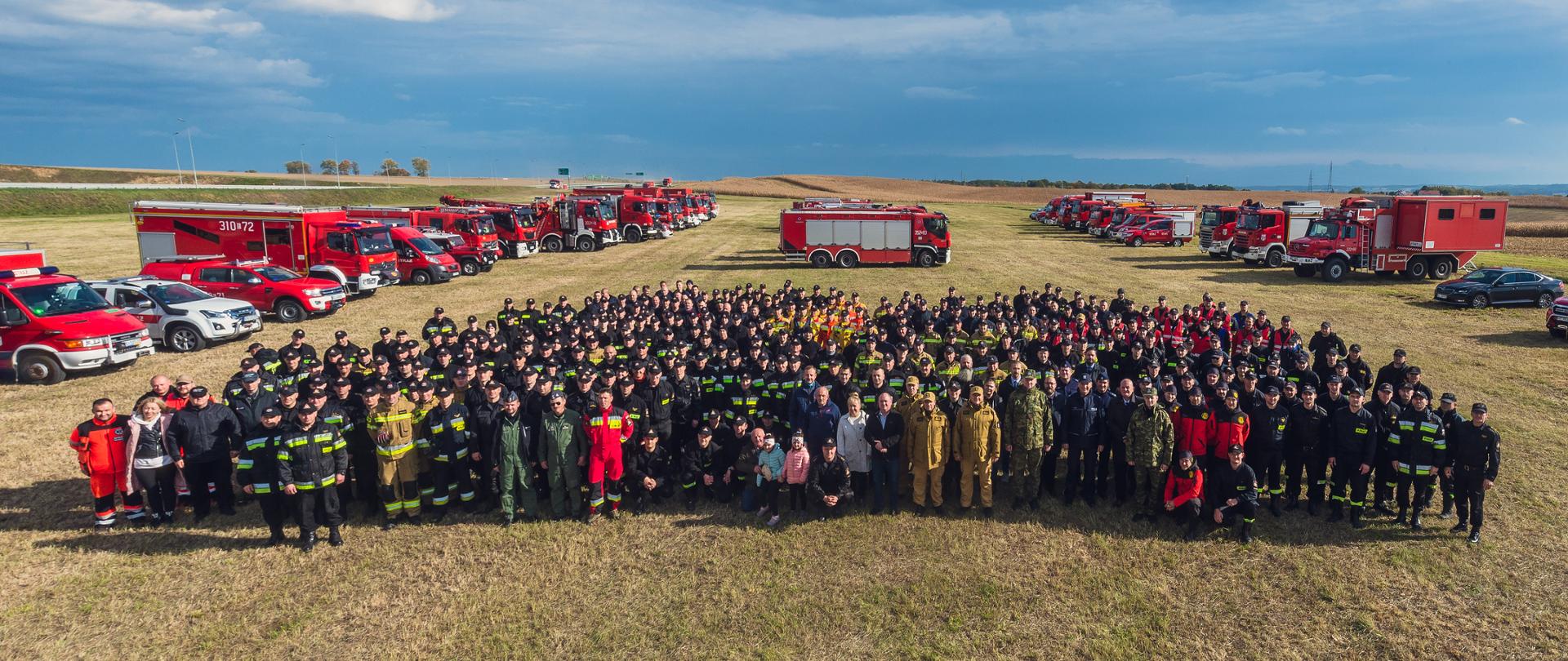 Zdjęcie pamiątkowe uczestników ćwiczeń, na tle pojazdów pożarniczych