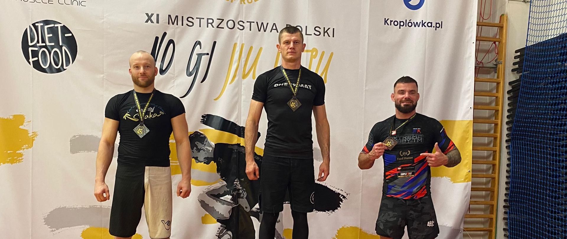 Trzech zawodników z medalami stoi na stopniach podium.