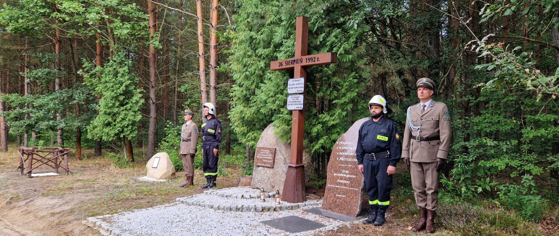 Na polanie w lesie, symboliczny krzyż upamietniajcy pożar lasu w Kużni Raciborskiej, obok niego warty druhów ochotniczej straży pożarnej i leśników.