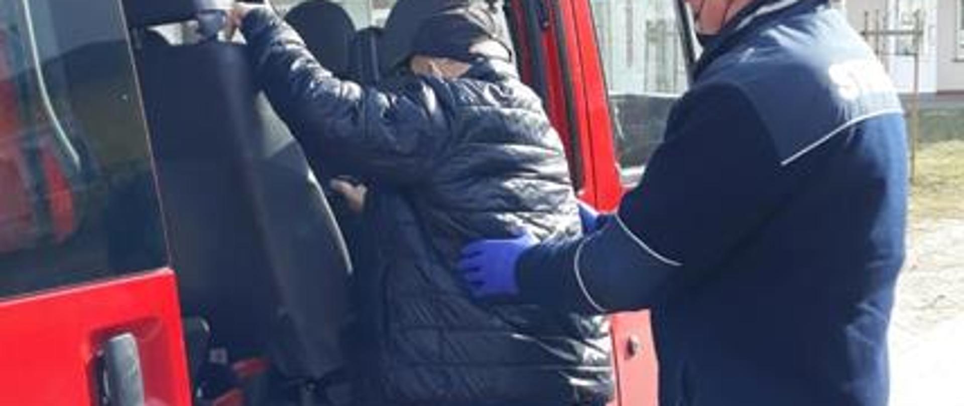 Strażak ratownik zabezpiecza starszą osobę wsiadającą do pojazdu pożarniczego