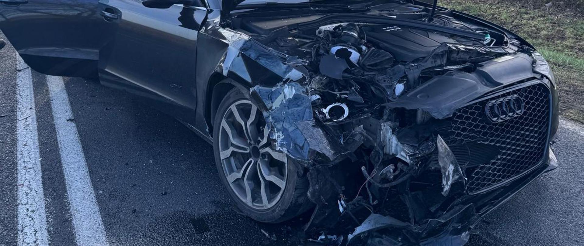 Uszkodzony samochód osobowy koloru czarnego przy nim strażacy 