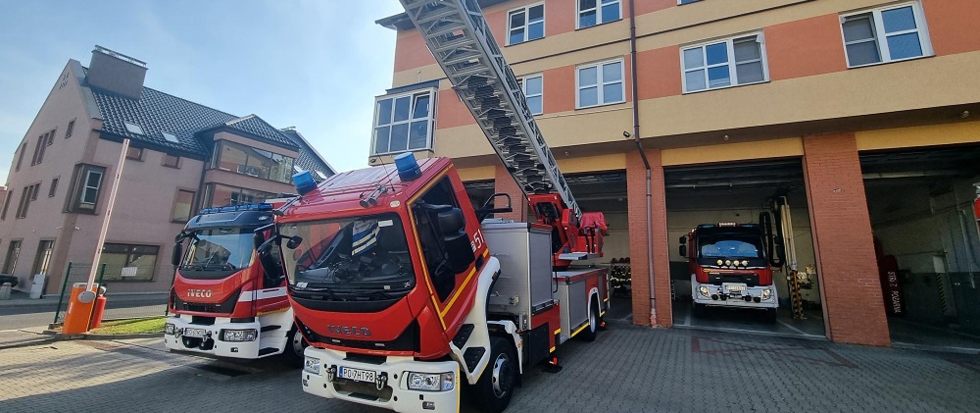 Zdjęcie przedstawia strażaków sprawdzających sprzęt techniczny pożarniczy.
W tle budynek Komendy i pojazdy pożarnicze.
