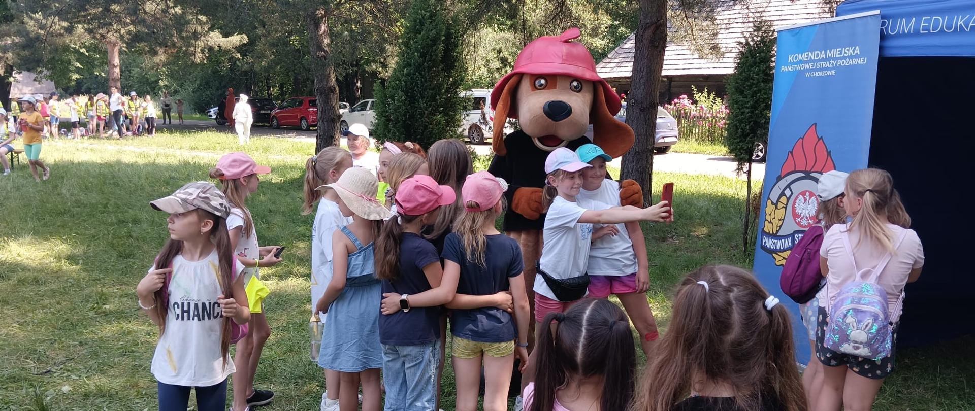 Zdjęcie przedstawia maskotkę "Psa Żarka" oraz grupę dzieci