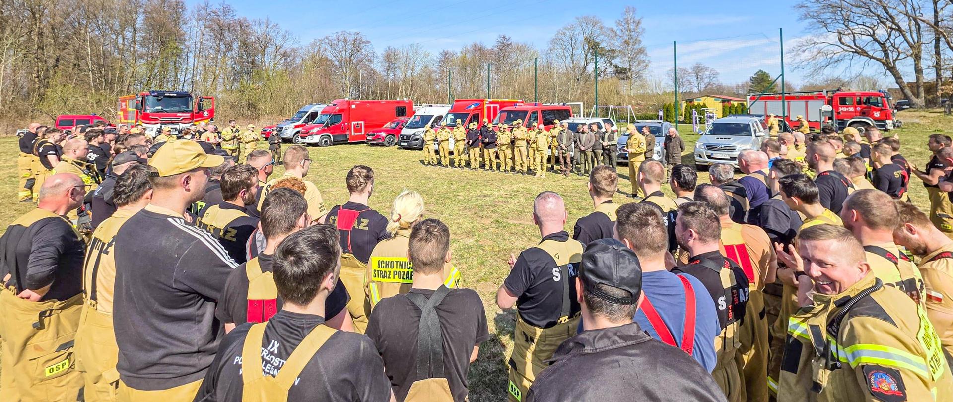Zdjęcie przedstawia uczestników ćwiczeń Koncentracja "CHARNOWO 2026", stojących na stadionie w tle pojazdy pożarnicze.