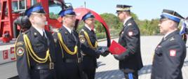 Powiatowe Obchody Dnia Strażaka 2023 - generał wręcza nagrody strażakowi który stoi w poczcie
