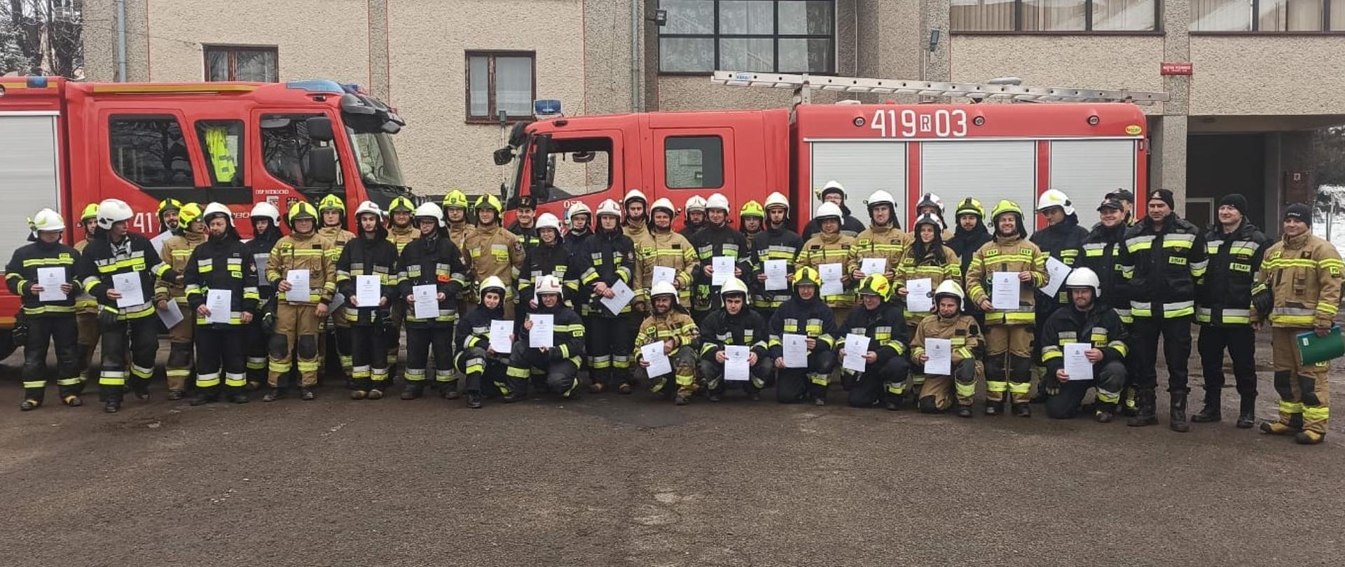 Zdjęcie przedstawia kursantów którzy ukończyli szkolenie. W tle remiza OSP w Starej Wsi oraz pojazdy gaśnicze